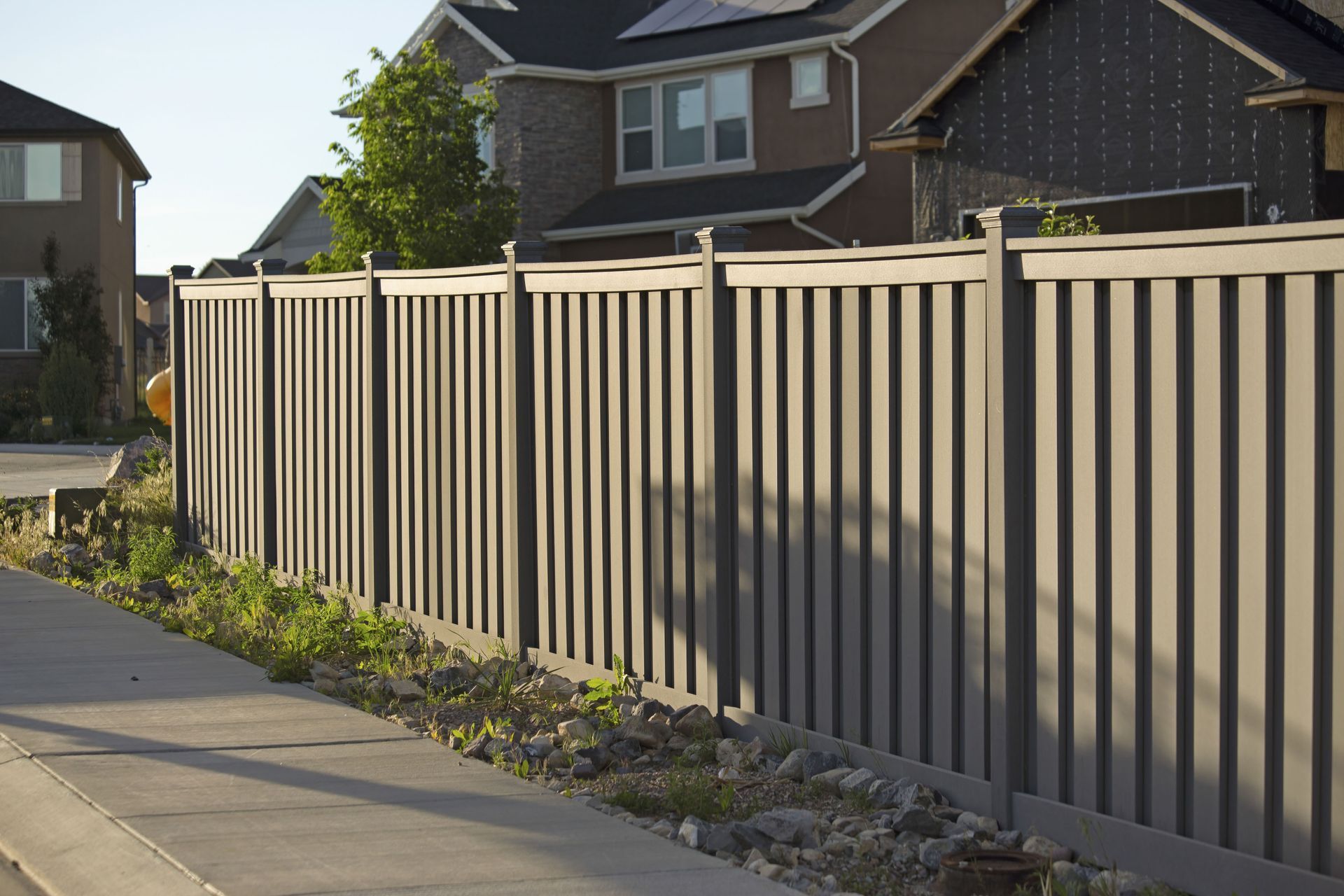 Beige metal fence along a sidewalk beside suburban houses in daylight