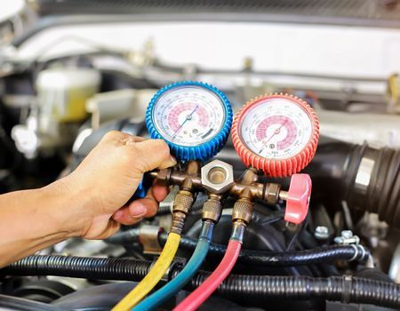 A person uses a gauge set to check car air conditioning system in an engine compartment. Blue and red gauges with attached hoses.