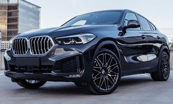 Black BMW X6 SUV parked outdoors, featuring a sleek, coupe-like roofline and sporty wheels, set against a modern building.