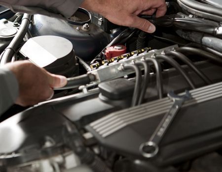 Mechanic working on a car engine, using tools in an engine bay. Focus on the hands and tools.