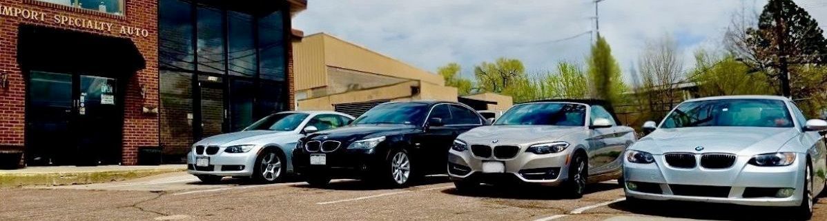 Four silver and black cars parked in front of a building with large windows, under a cloudy sky.
