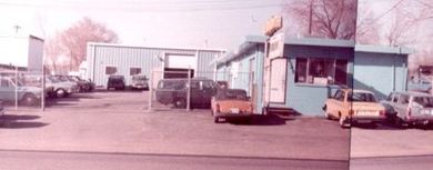 An auto repair shop with cars parked outside. The building is light blue, and a sign sits on top.