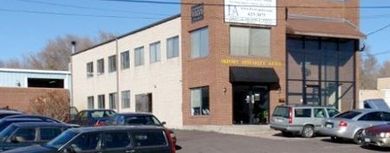 A two-story brick building with a black awning over the entrance and cars parked out front. There is a sign on the building as well.