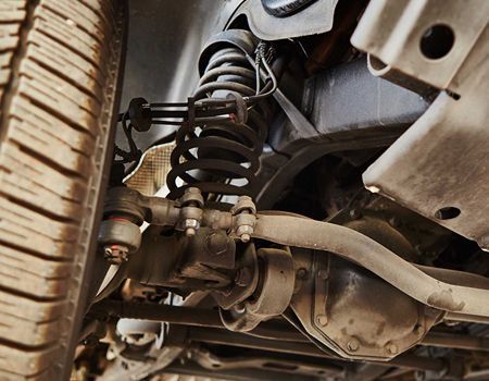 Close-up of a car's suspension system. Black spring, shock absorber, and associated linkages are visible under the vehicle.