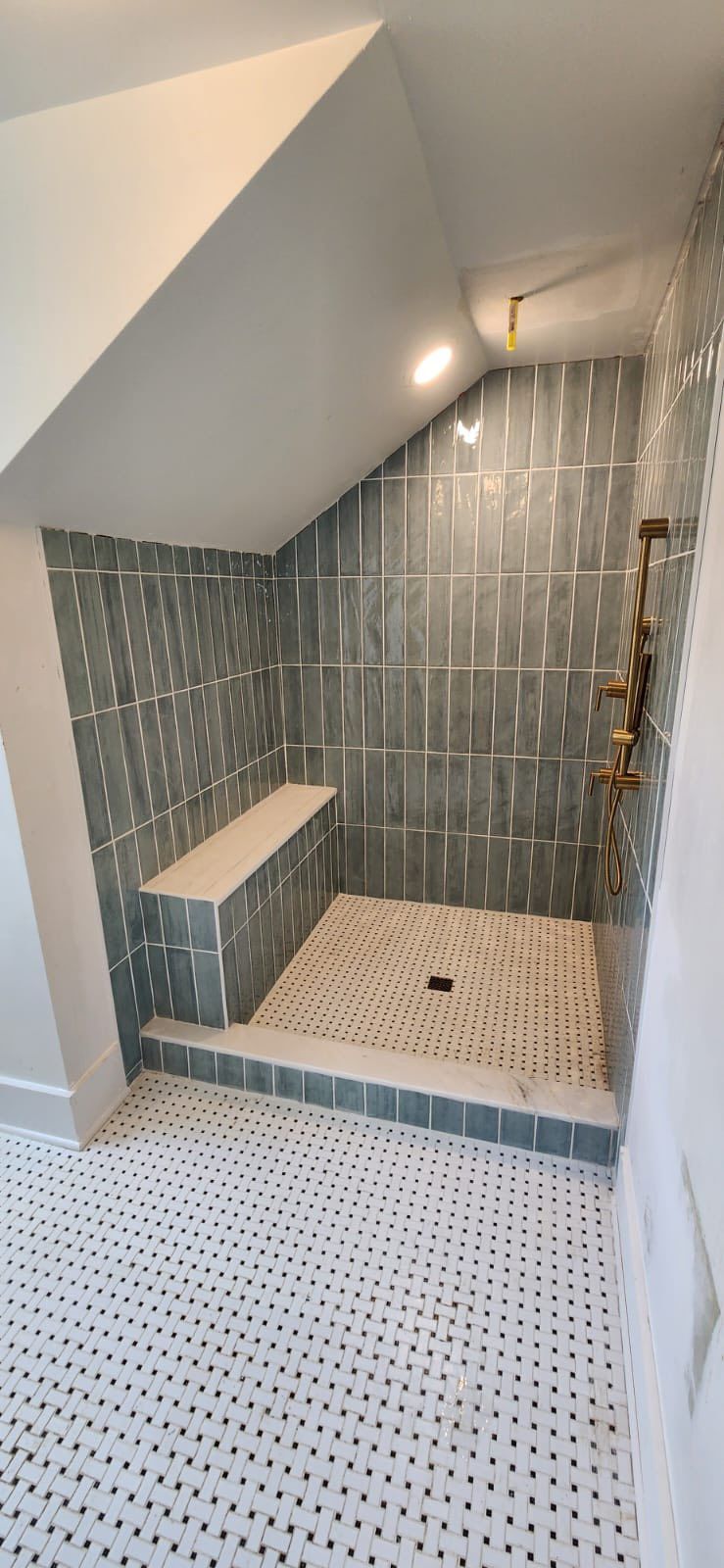 A bathroom shower with teal tiles on the walls and step, white mosaic tile floor, and a wooden bench.