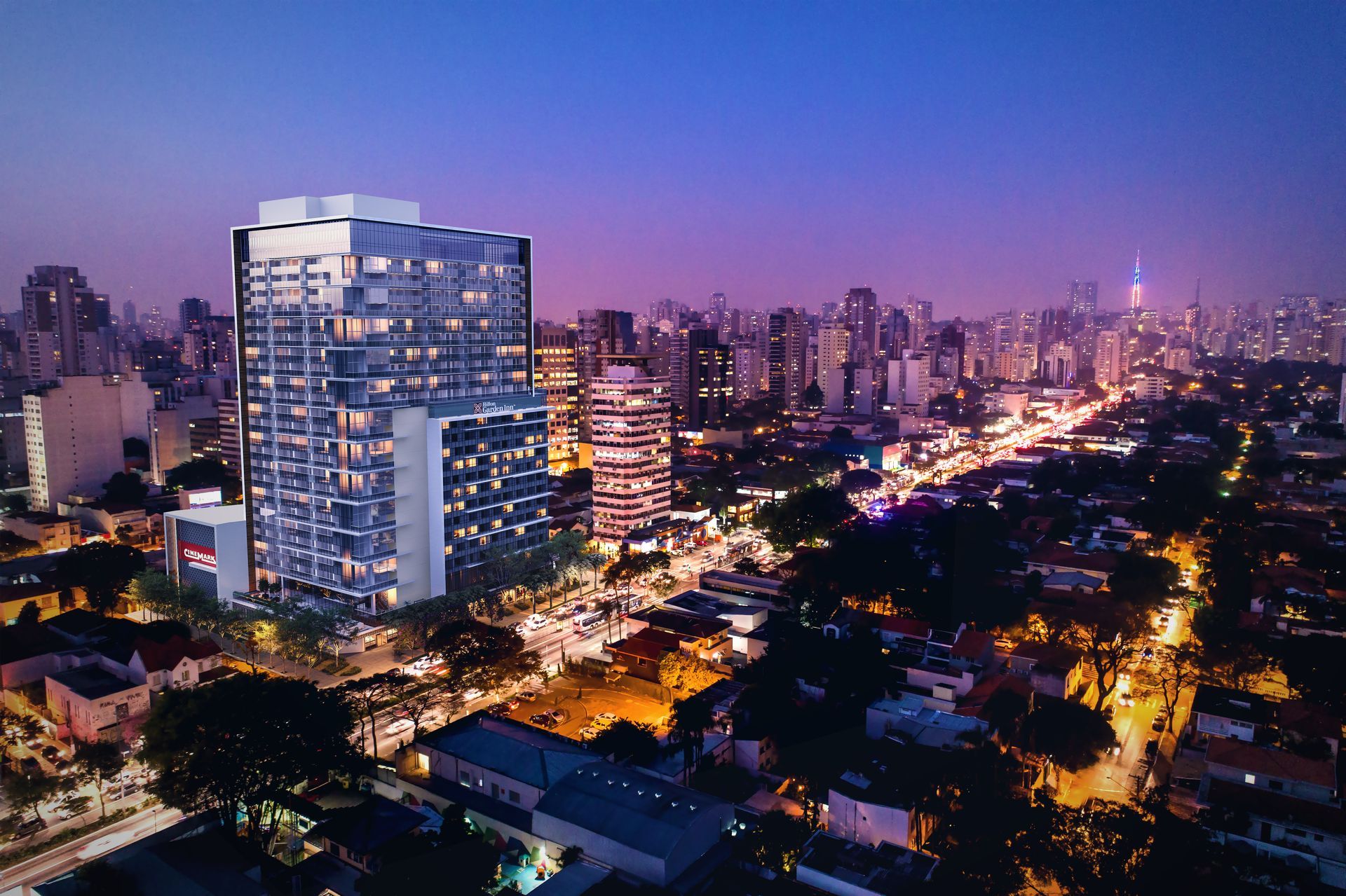 Uma vista aérea de uma cidade à noite com um grande edifício em primeiro plano.