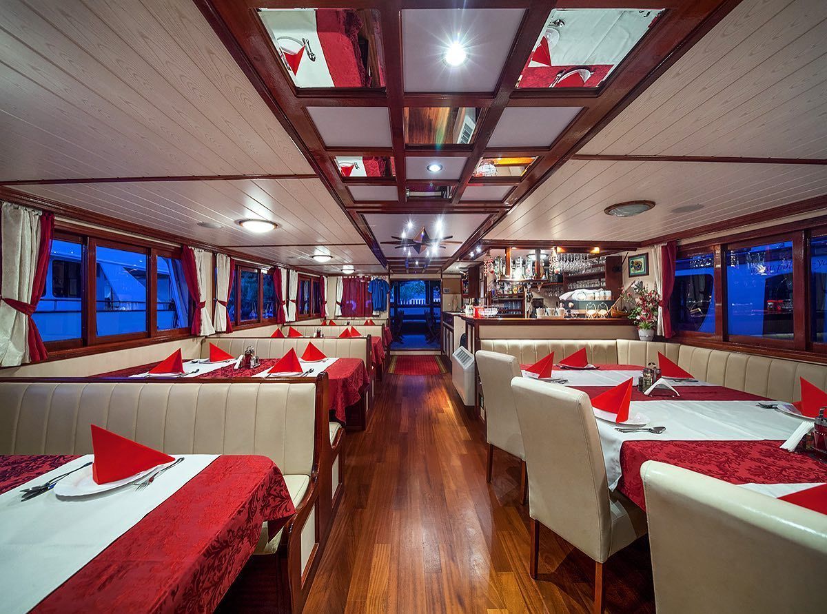 Interior of a restaurant on a boat with red accents. Tables set for dining with a bar in the back.