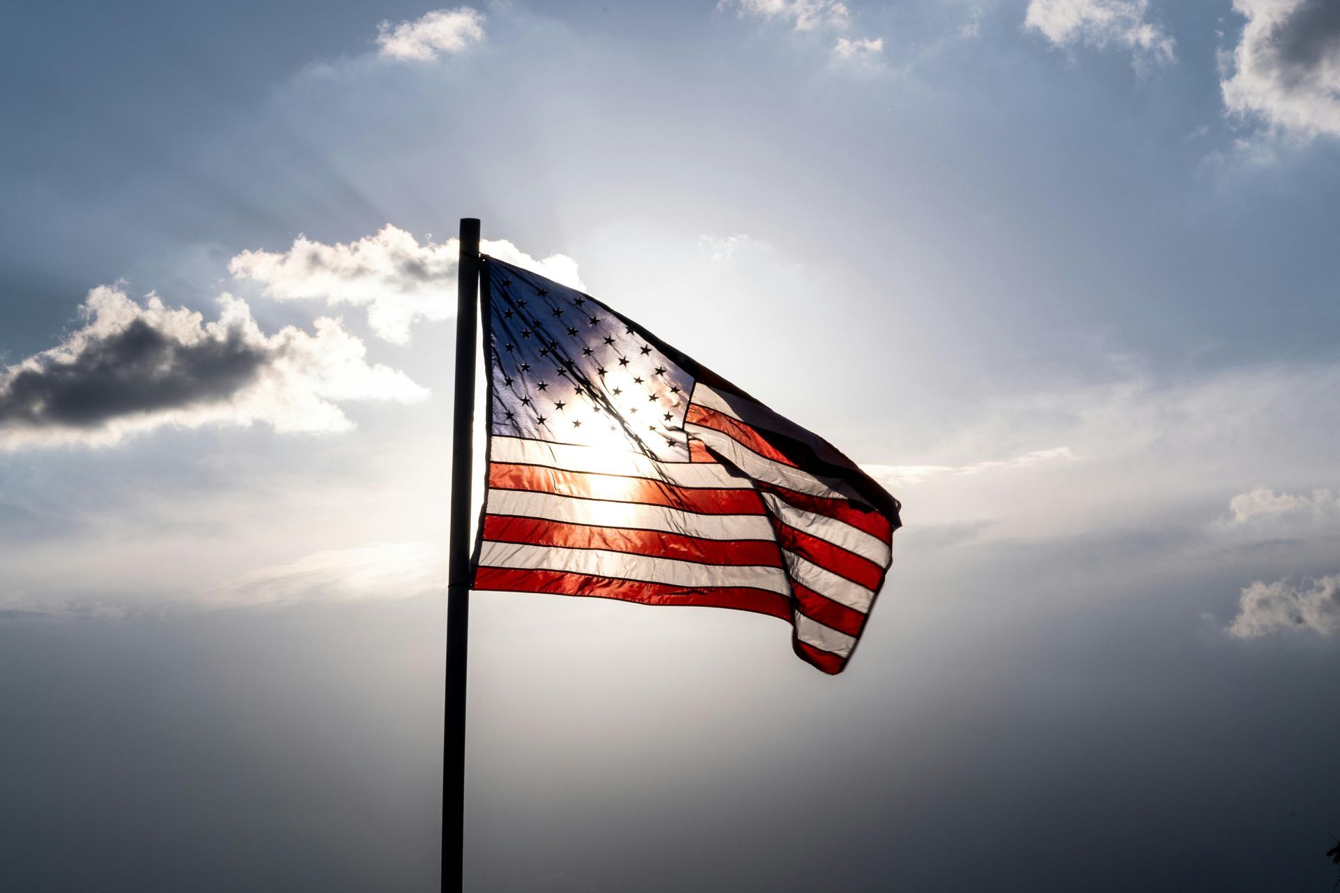 American flag waving against a bright sun and cloudy sky.