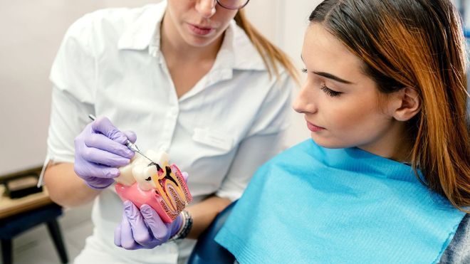 Una donna è seduta sulla poltrona del dentista mentre un dentista le esamina i denti.