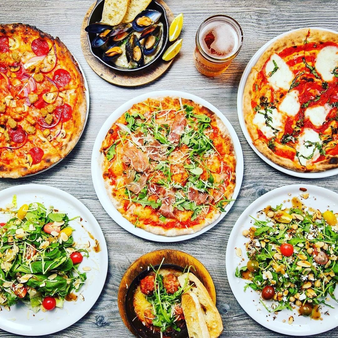 There are many different types of pizzas and salads on the table.