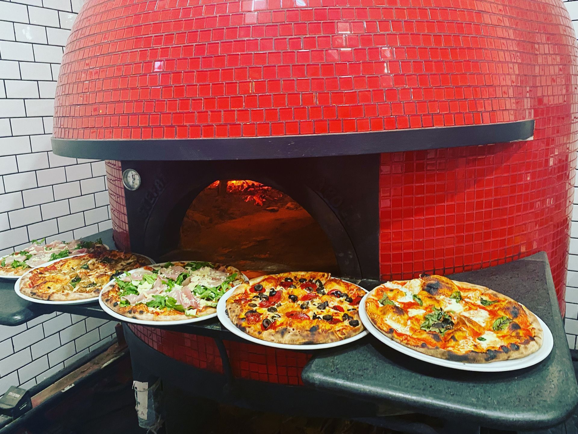 A row of pizzas sitting on a table in front of a red brick oven.