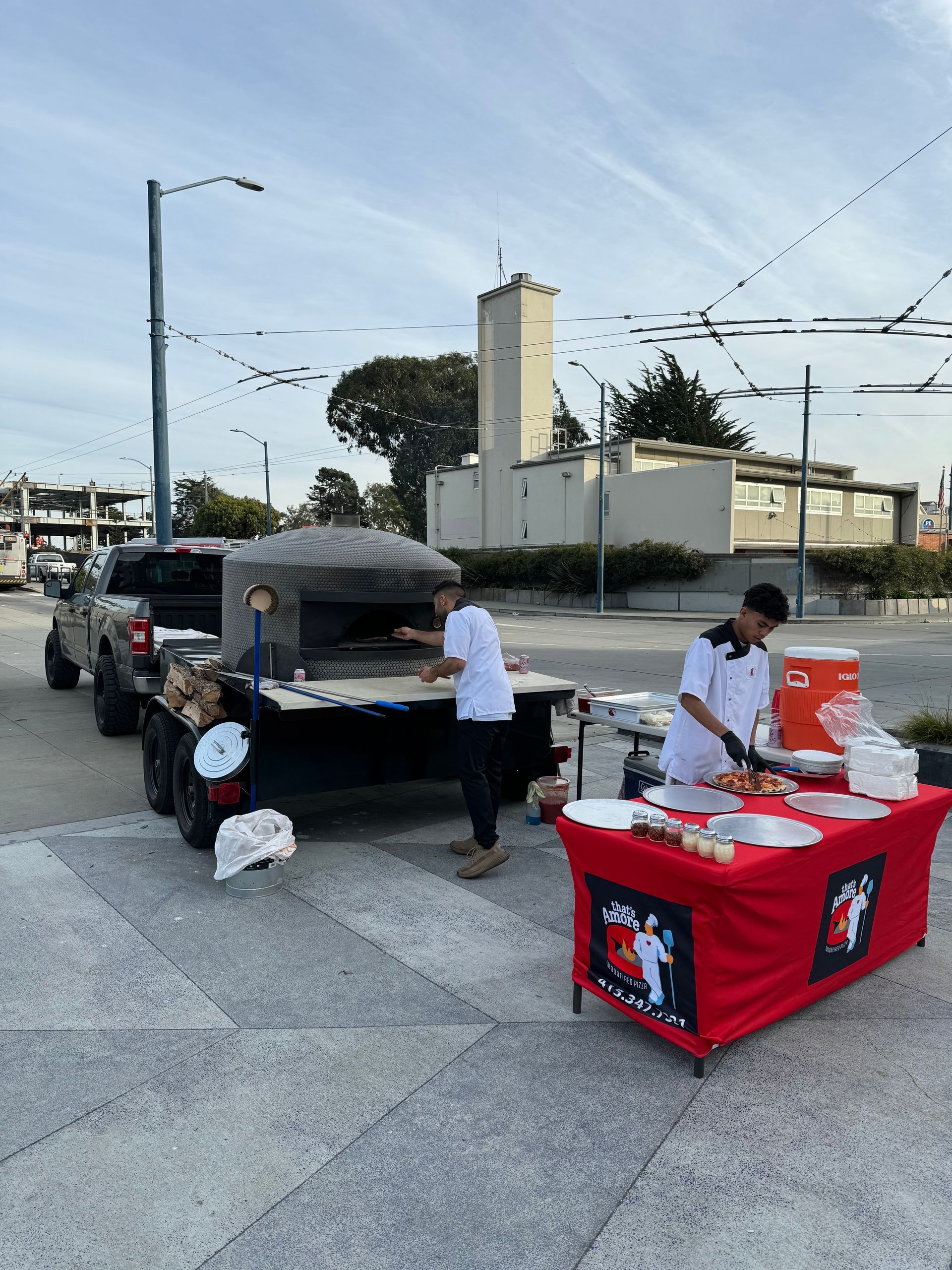 A man is standing in front of a pizza oven in a parking lot.