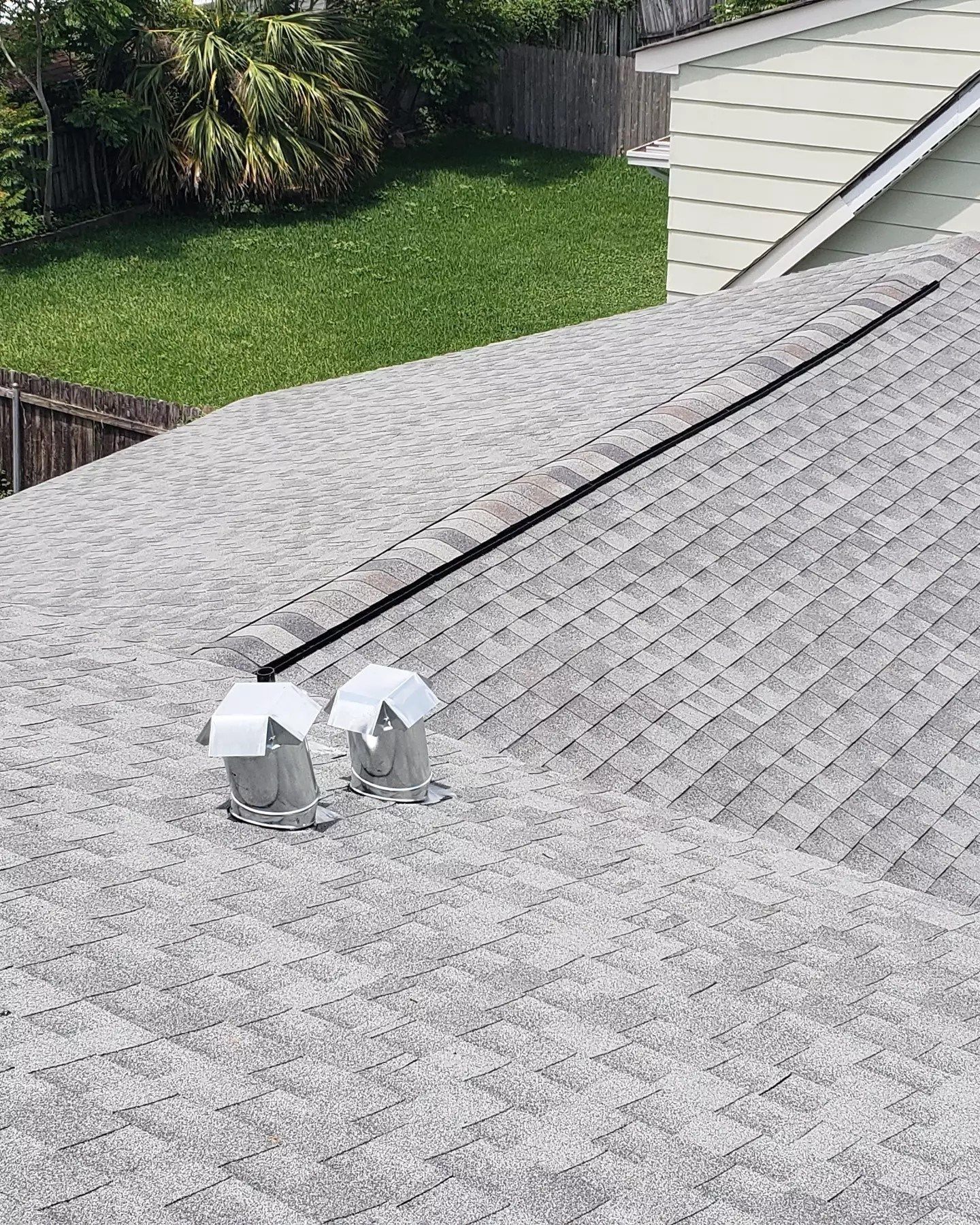 Gray shingled roof with two silver roof vents and a black cable, beside a green lawn and house siding