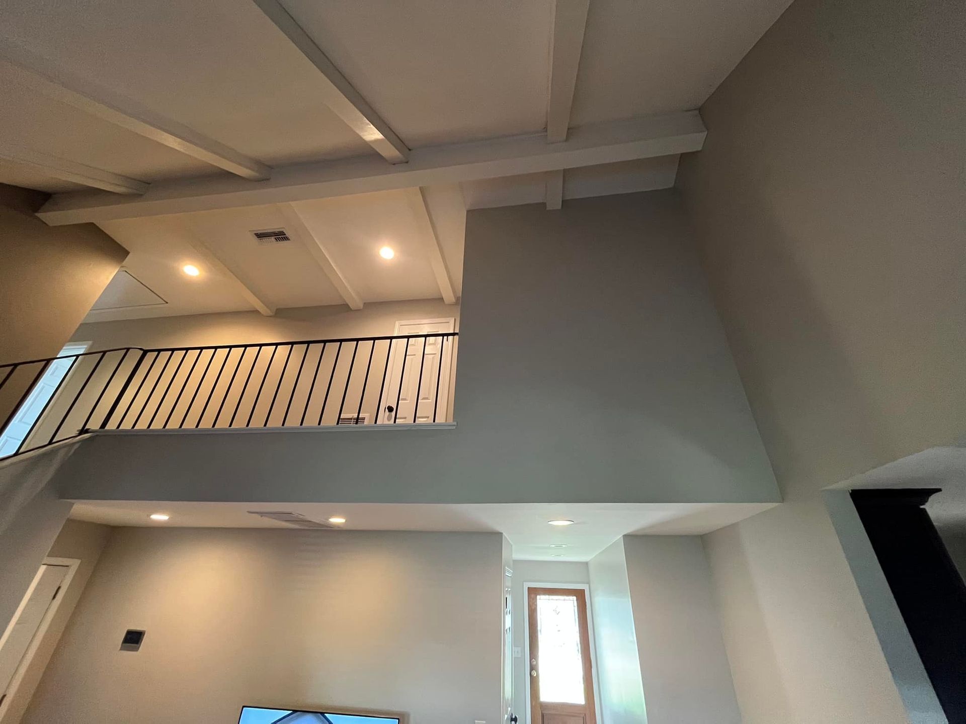 Modern interior with high ceiling, loft balcony railing, recessed lights, and a small door below