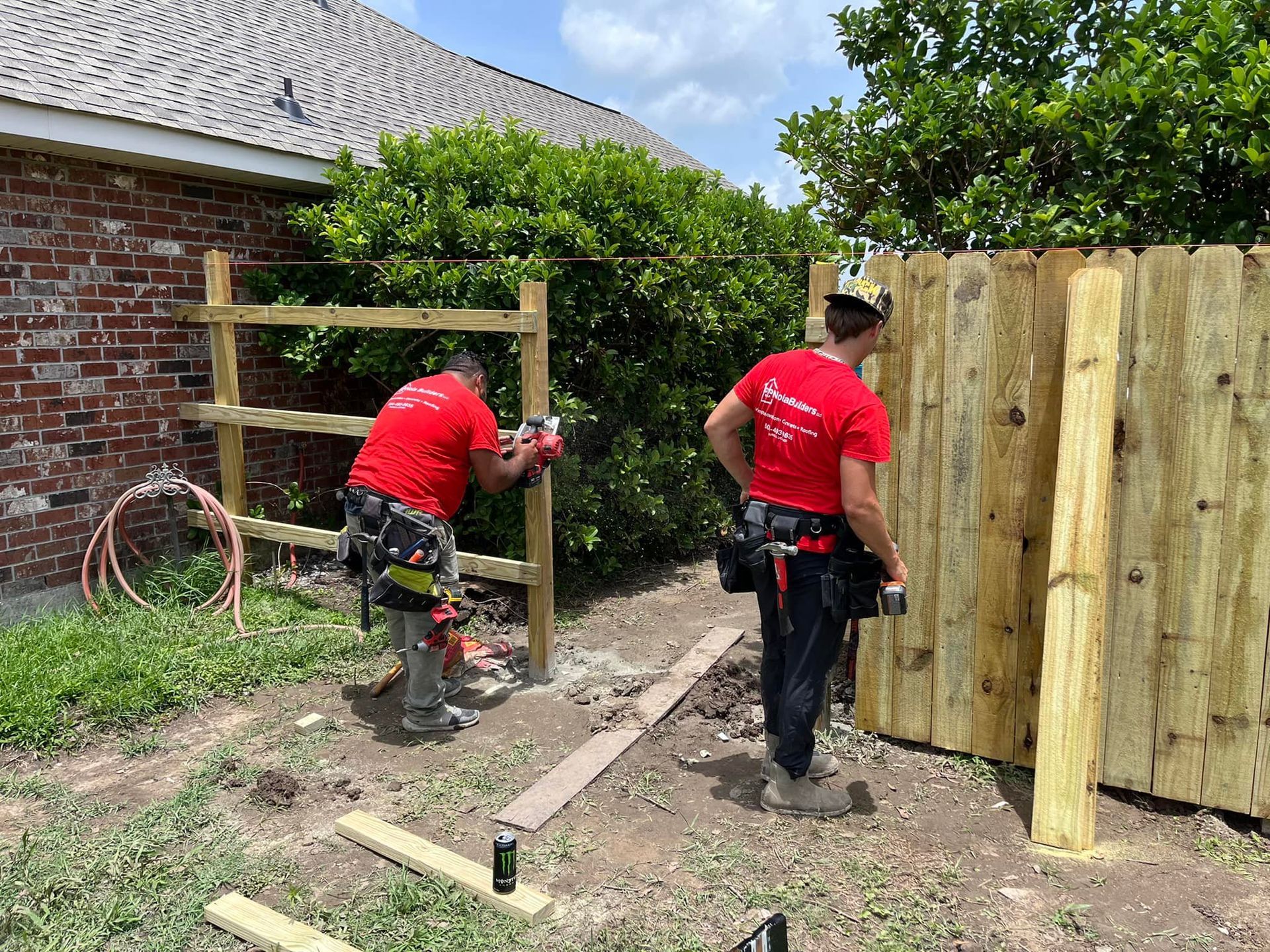 Two workers in red shirts installing a wooden fence in a backyard.
