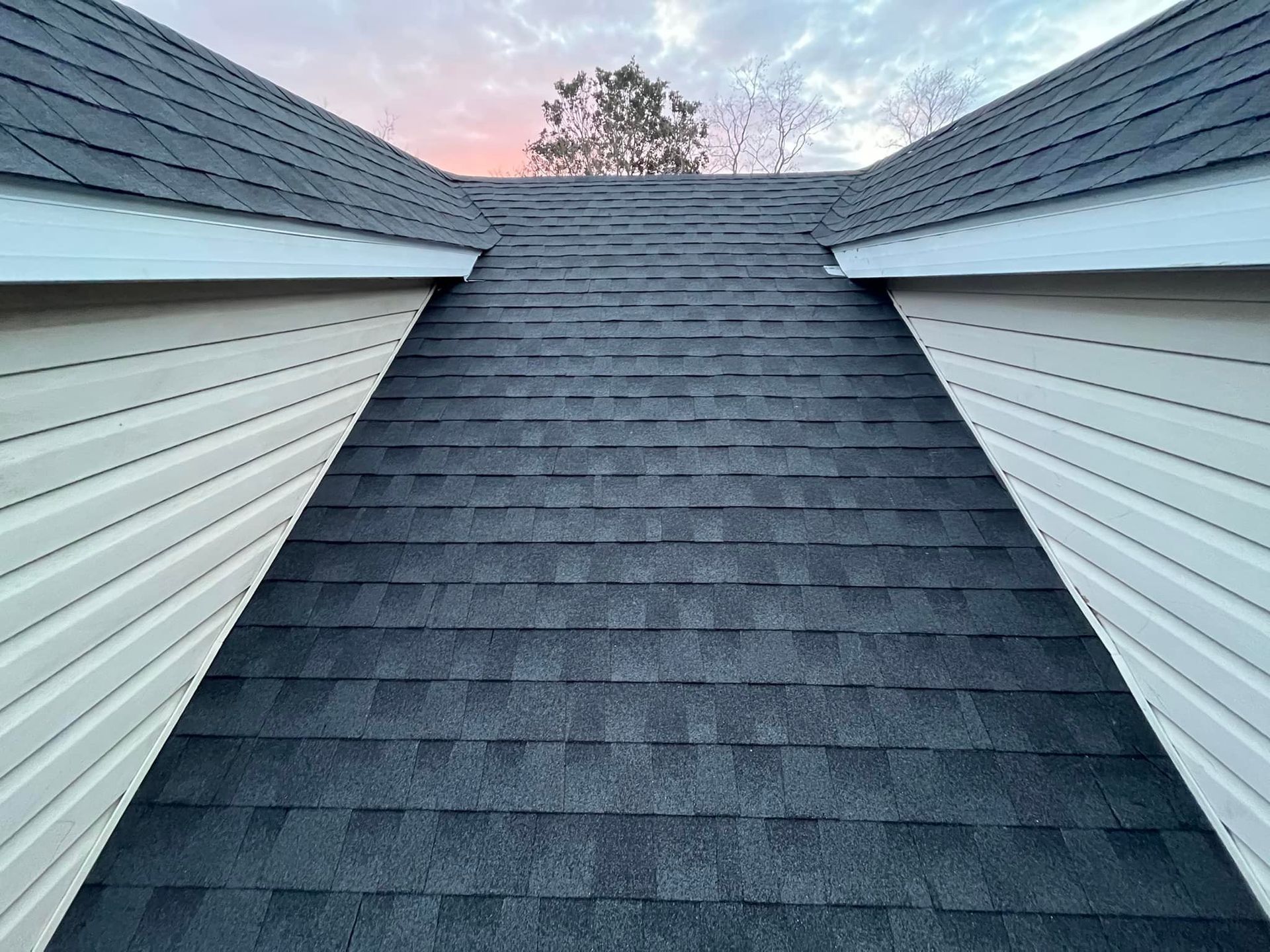 Steep dark gray roof framed by white siding against a pink evening sky
