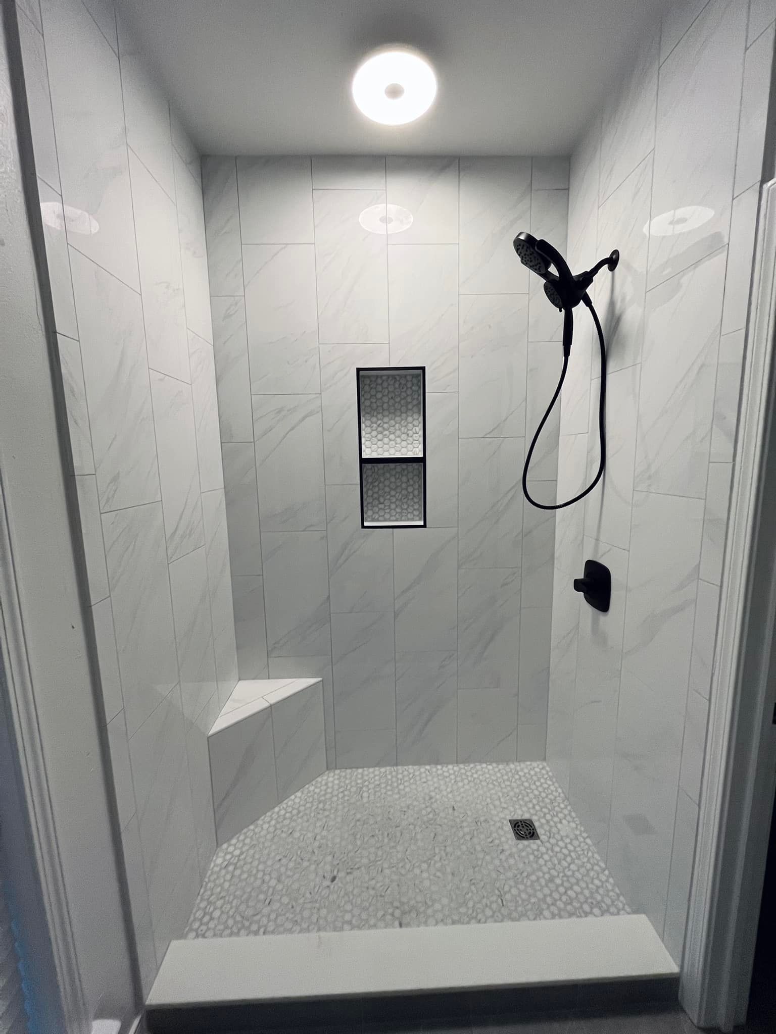 Empty tiled shower stall with rainfall showerhead and built-in shelf, viewed from the entrance.