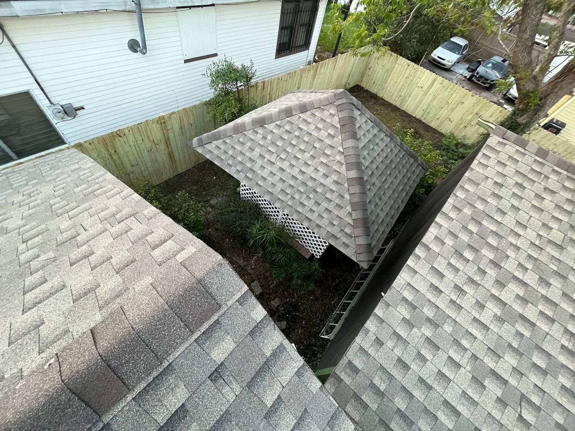 Overhead view of a fenced backyard with two shingled sheds and a parked car nearby