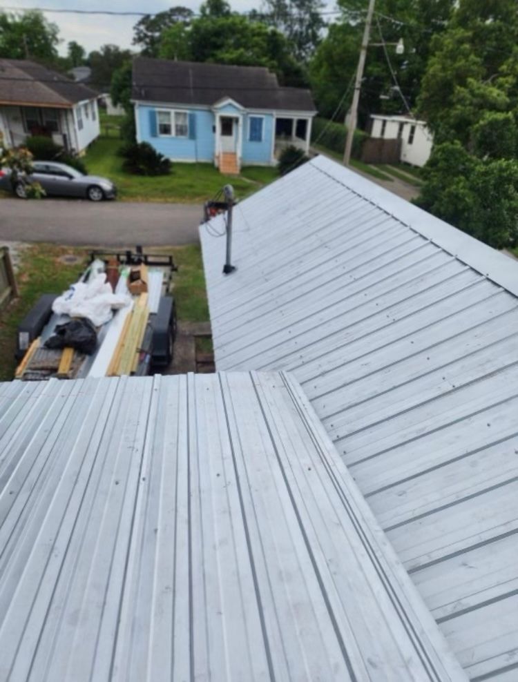 Roofing work on a metal roof, with workers and materials visible below on a residential street.