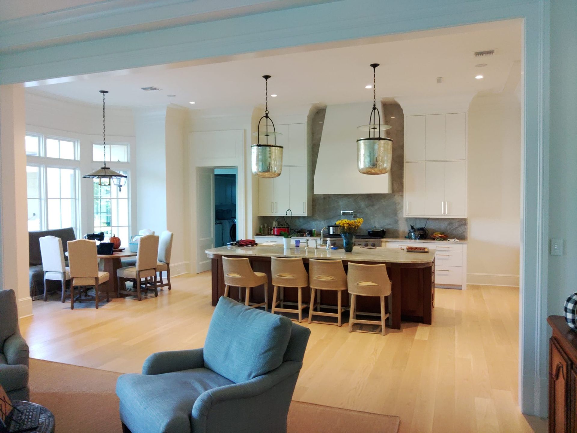 Open-plan modern kitchen and dining area with light wood floors and blue seating, viewed through a wide doorway