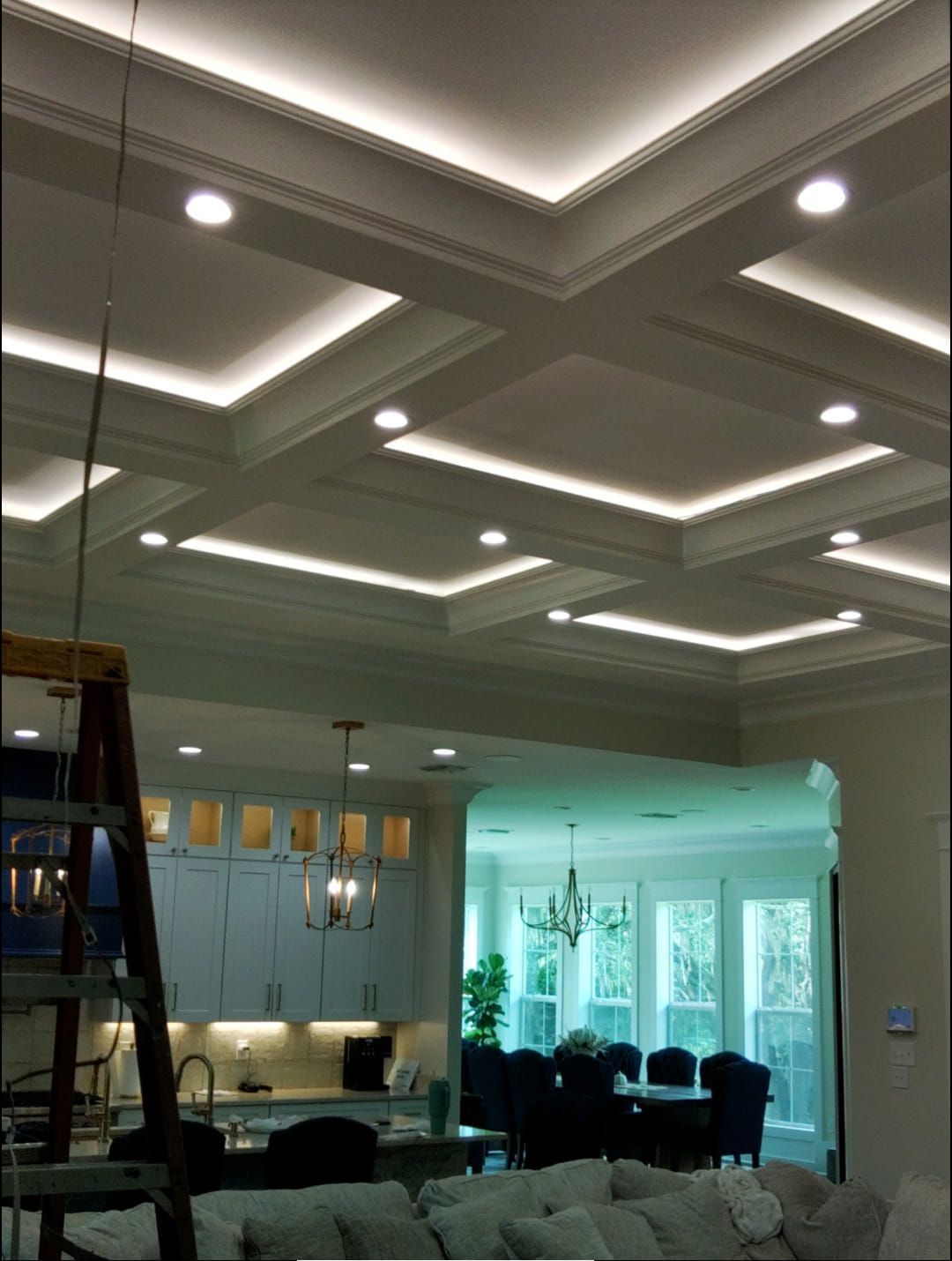 Modern living room with tray ceiling, recessed lights, pendant lamps, and dark seating near large windows