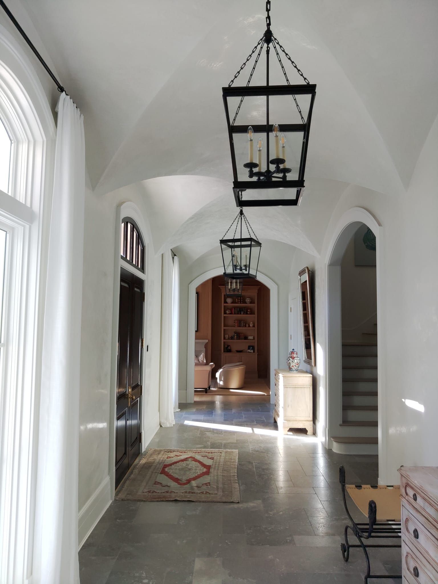 Bright white arched hallway with hanging lanterns, stone floor, and a sunlit doorway at the end