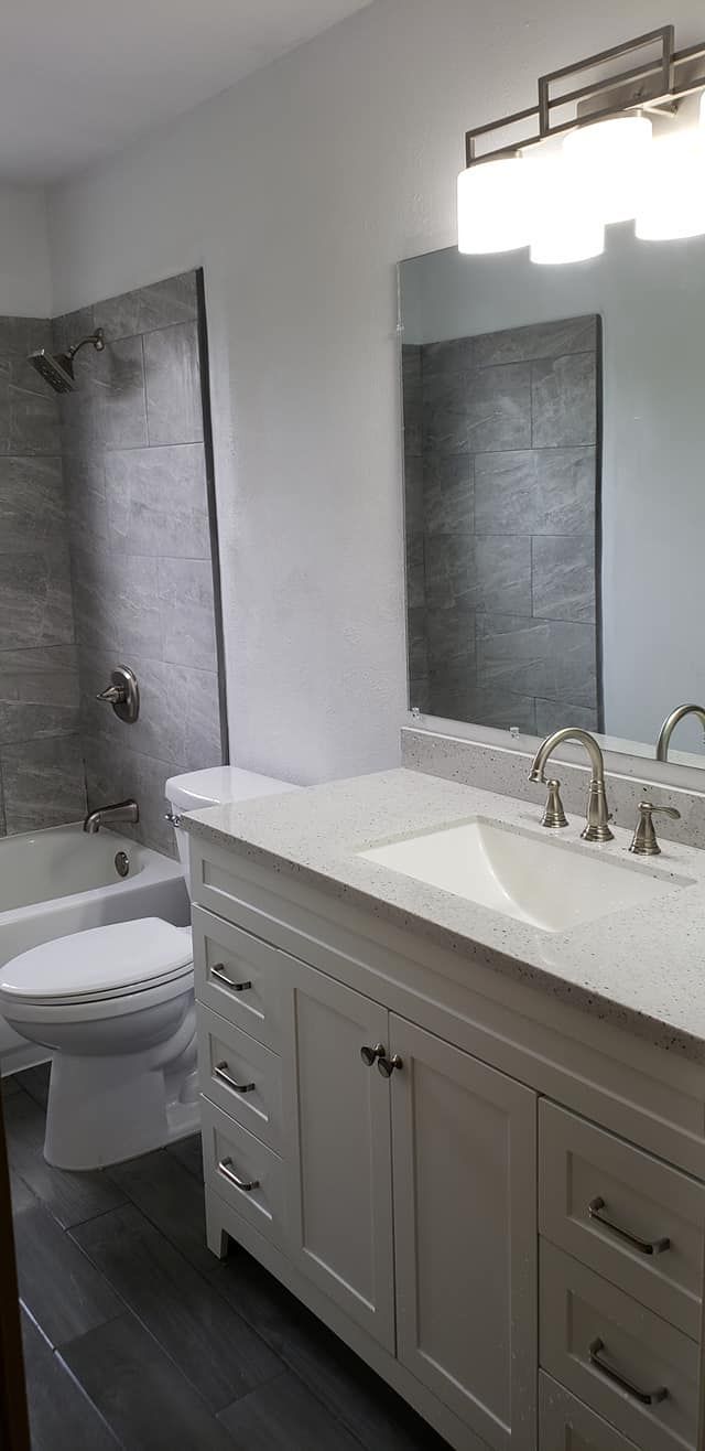 Modern bathroom with white vanity, marble countertop, mirror, and toilet beside a shower stall.