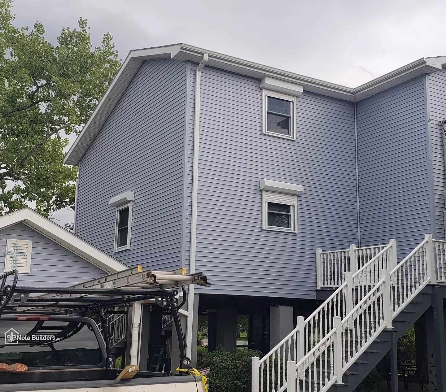 Blue-gray house exterior with white trim, outdoor stairs, and a vehicle lift in the foreground