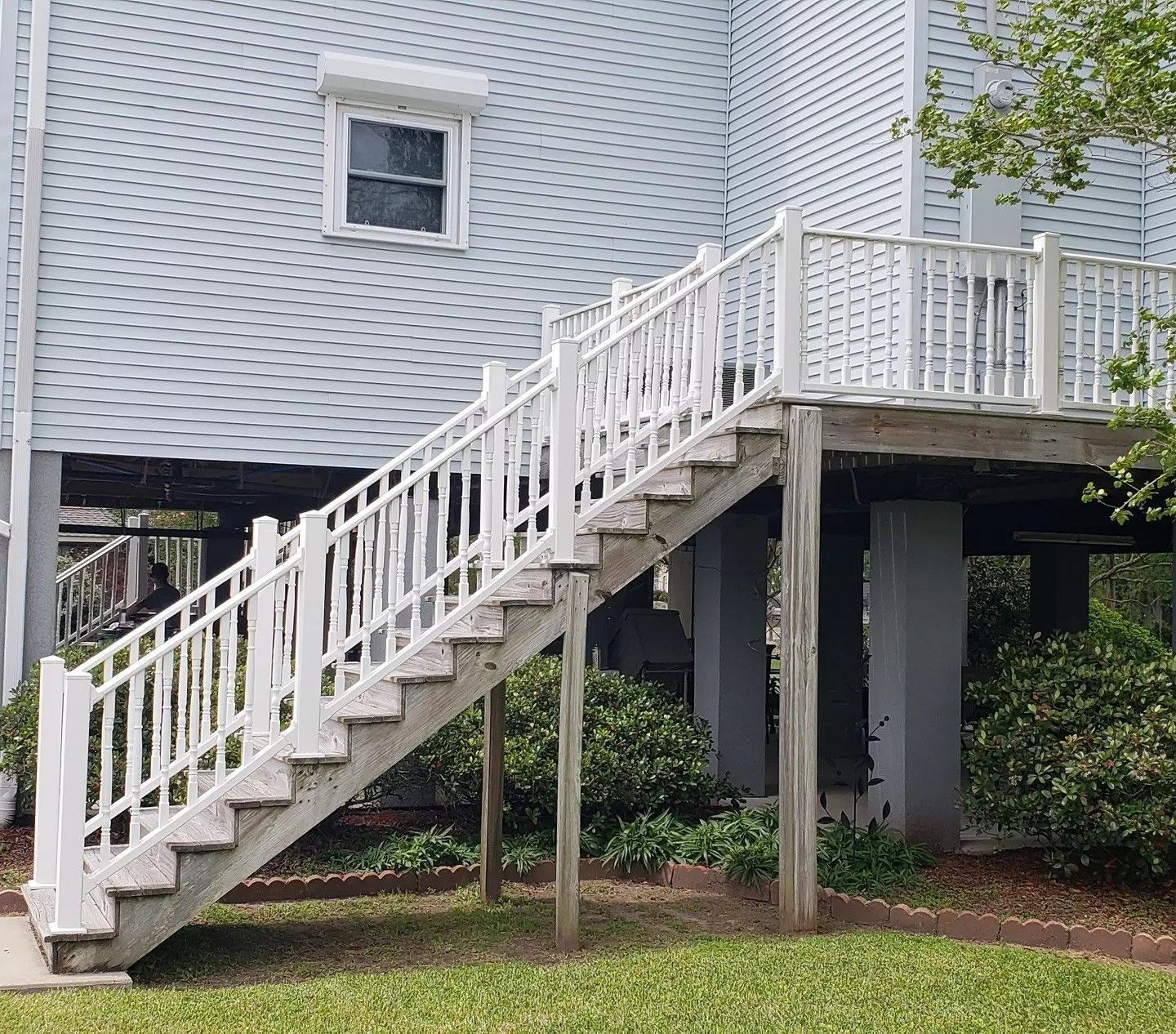 White exterior staircase leading to a raised house with a small window and porch railing