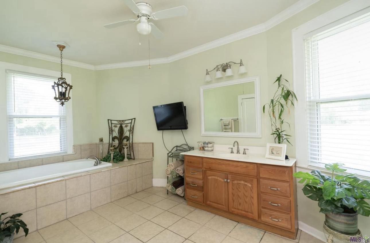 Bright bathroom with white tile, wood vanity, mirror, wall TV, and large windows.