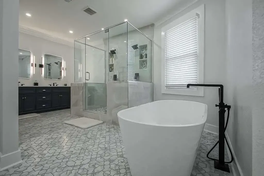 Bright modern bathroom with freestanding tub, glass shower, patterned tile floor, and black vanity