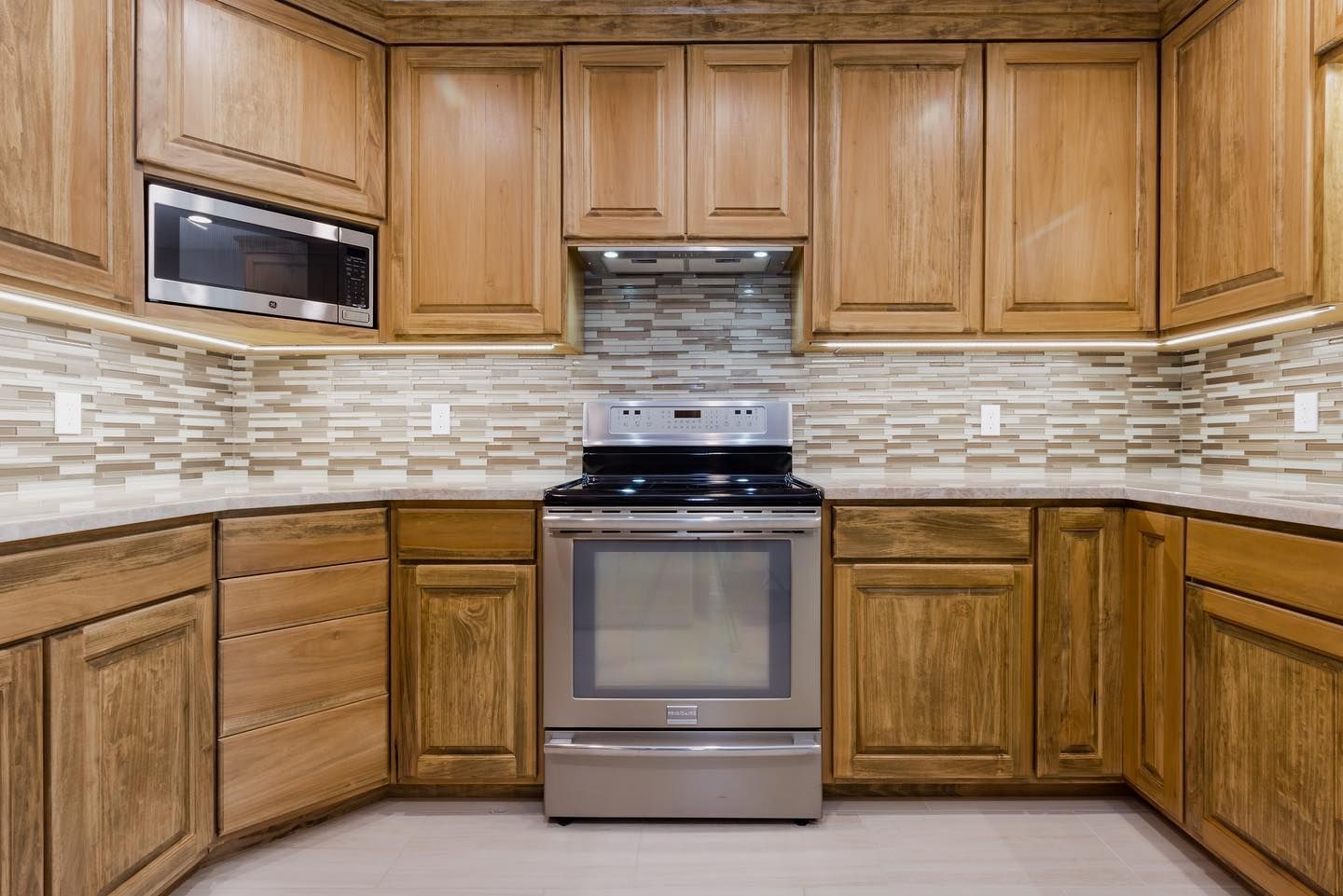 Kitchen with wooden cabinets, stainless steel stove, built-in microwave, and tiled backsplash.