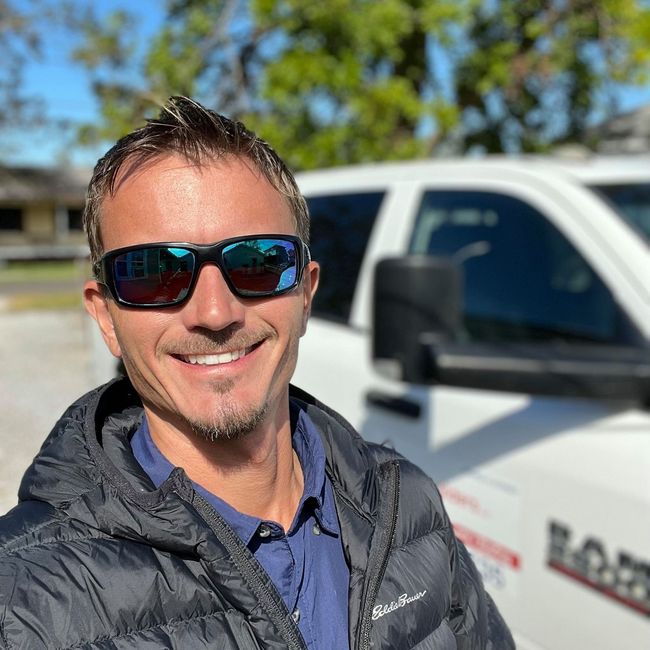Caleb Hensley of Nola Builders in sunglasses taking a selfie beside a white truck outdoors on a sunny day