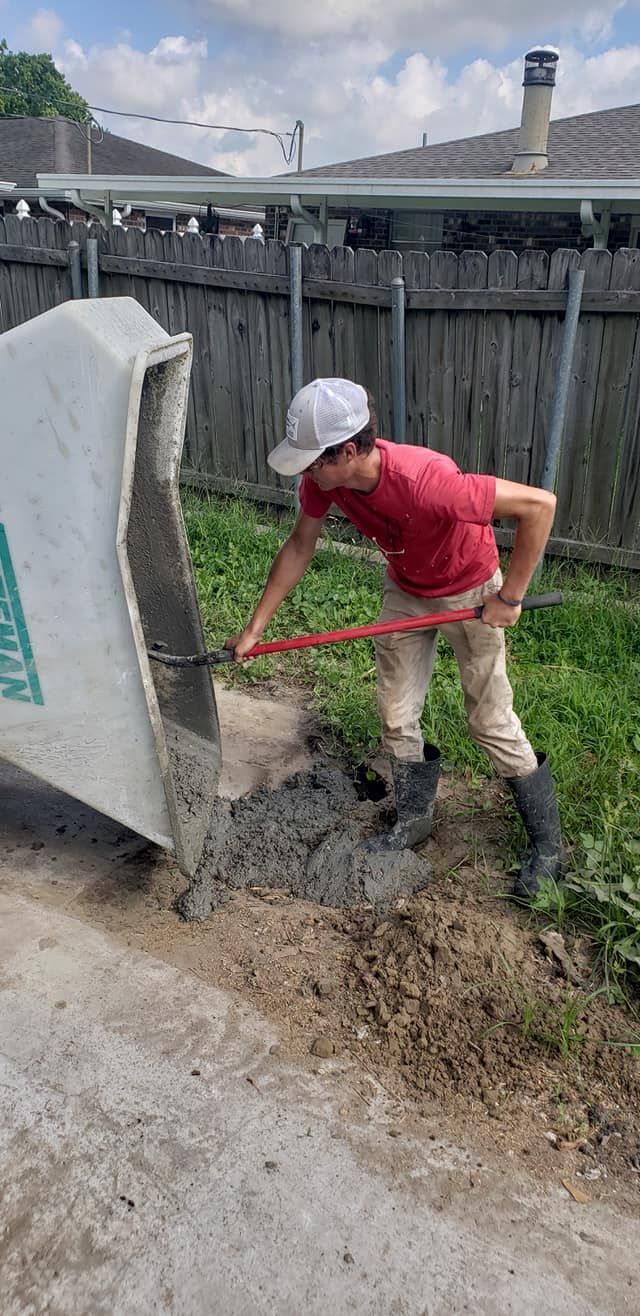Person in a red shirt digging wet soil beside a broken concrete fence post near a roadside.