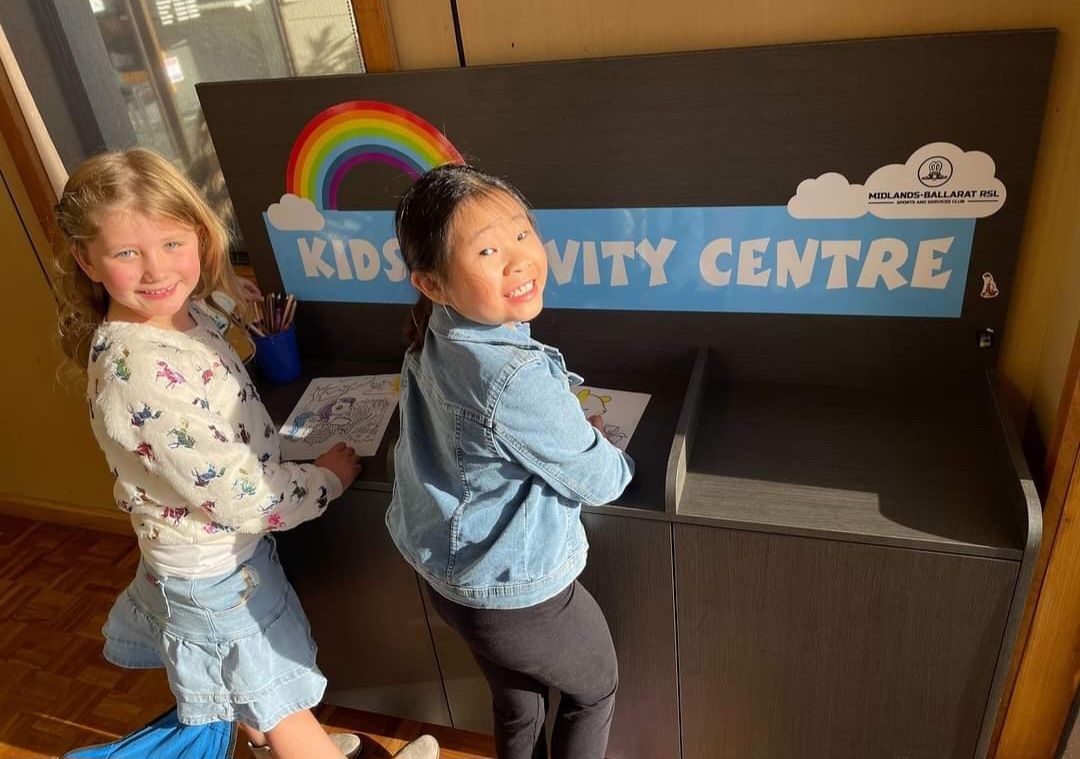 two girls coloring in front of a sign that says kids activity centre