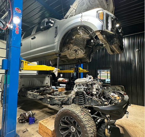 Silver SUV lifted over a dismantled engine and frame in an auto repair shop | Pro Import Automotive Service and Repair