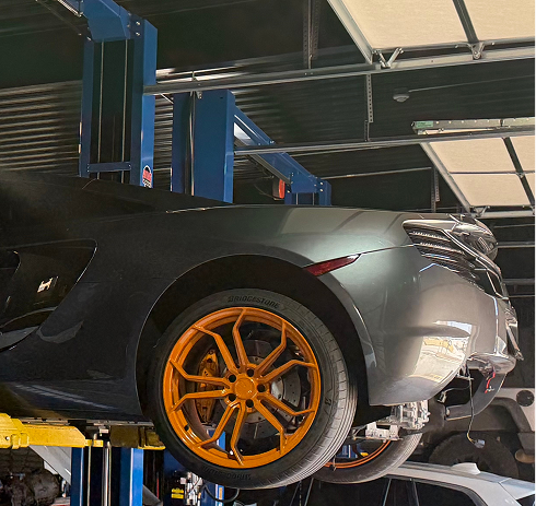 Black car on a lift in an auto shop, with bright orange wheels. | Pro Import Automotive Service and Repair