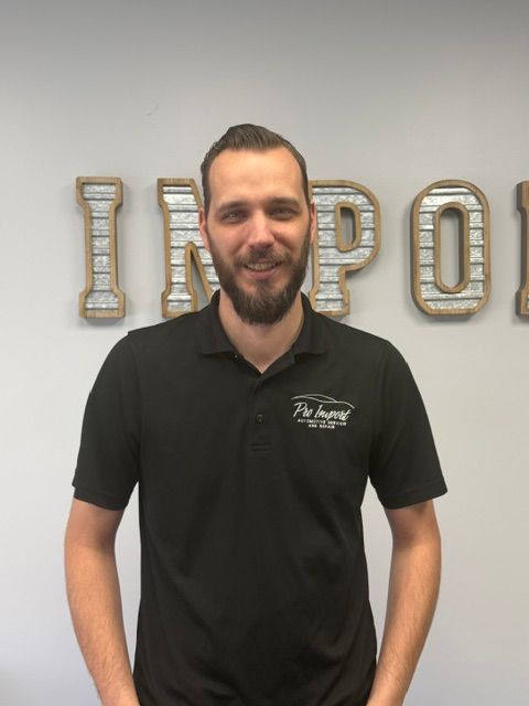 Man standing in a black polo shirt in front of an office wall| Pro Import Automotive Service and Repair