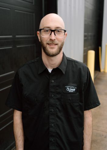 A person wearing glasses and a black uniform shirt. | Pro Import Automotive Service and Repair
