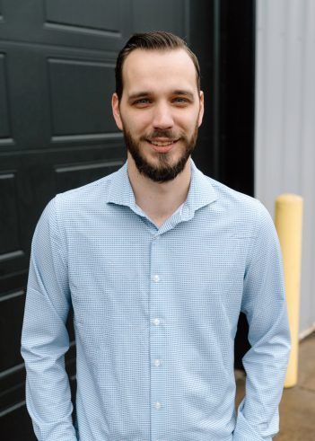 A person with a beard and short hair, smiles while standing outdoors. | Pro Import Automotive Service and Repair