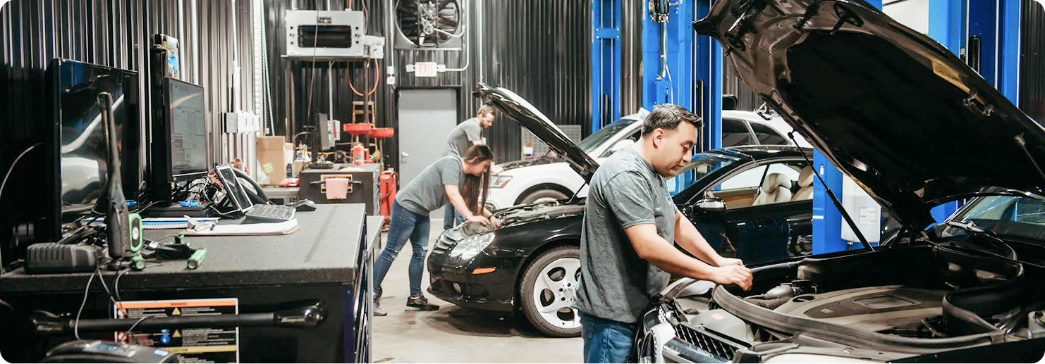 Two mechanics in a garage working under the open hoods of parked vehicles. | Pro Import Automotive Service and Repair