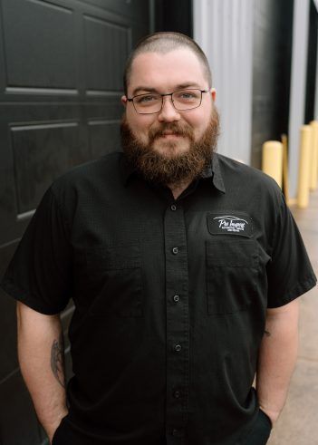 A bearded person with glasses wearing a black button-down shirt. | Pro Import Automotive Service and Repair