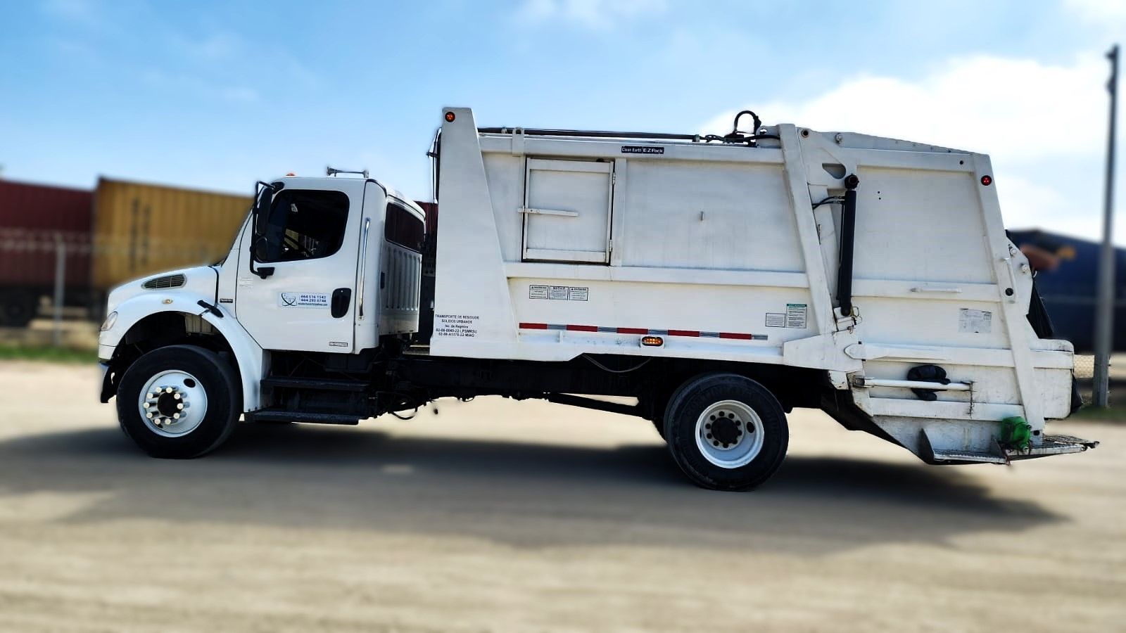 Un camión de basura blanco está estacionado en un camino de tierra
