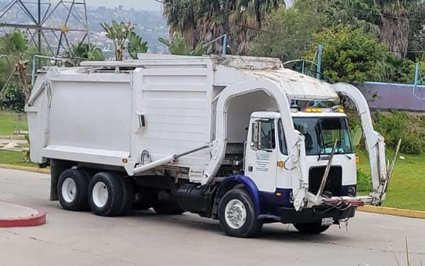 Un camión de basura blanco está estacionado al costado de la carretera.