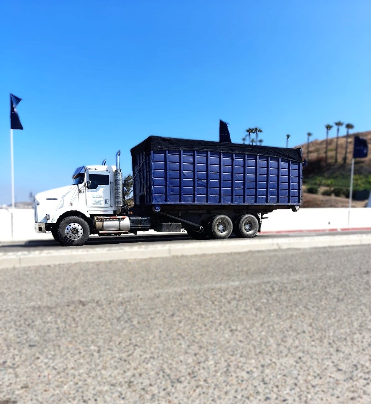 Un camión blanco con un remolque azul conduce por la carretera