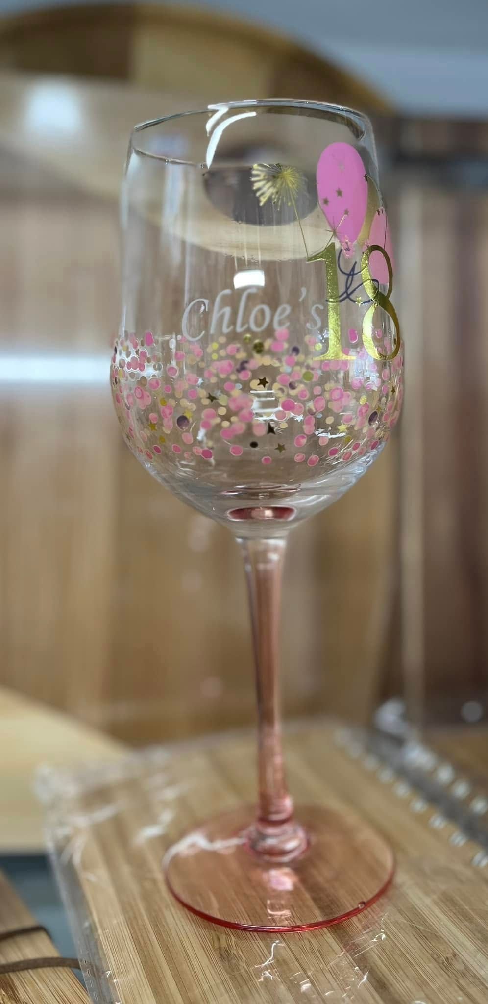 A Wine Glass With a Pink Stem is Sitting on a Wooden Table — Jimani Trophies & Engraving In Dapto, NSW