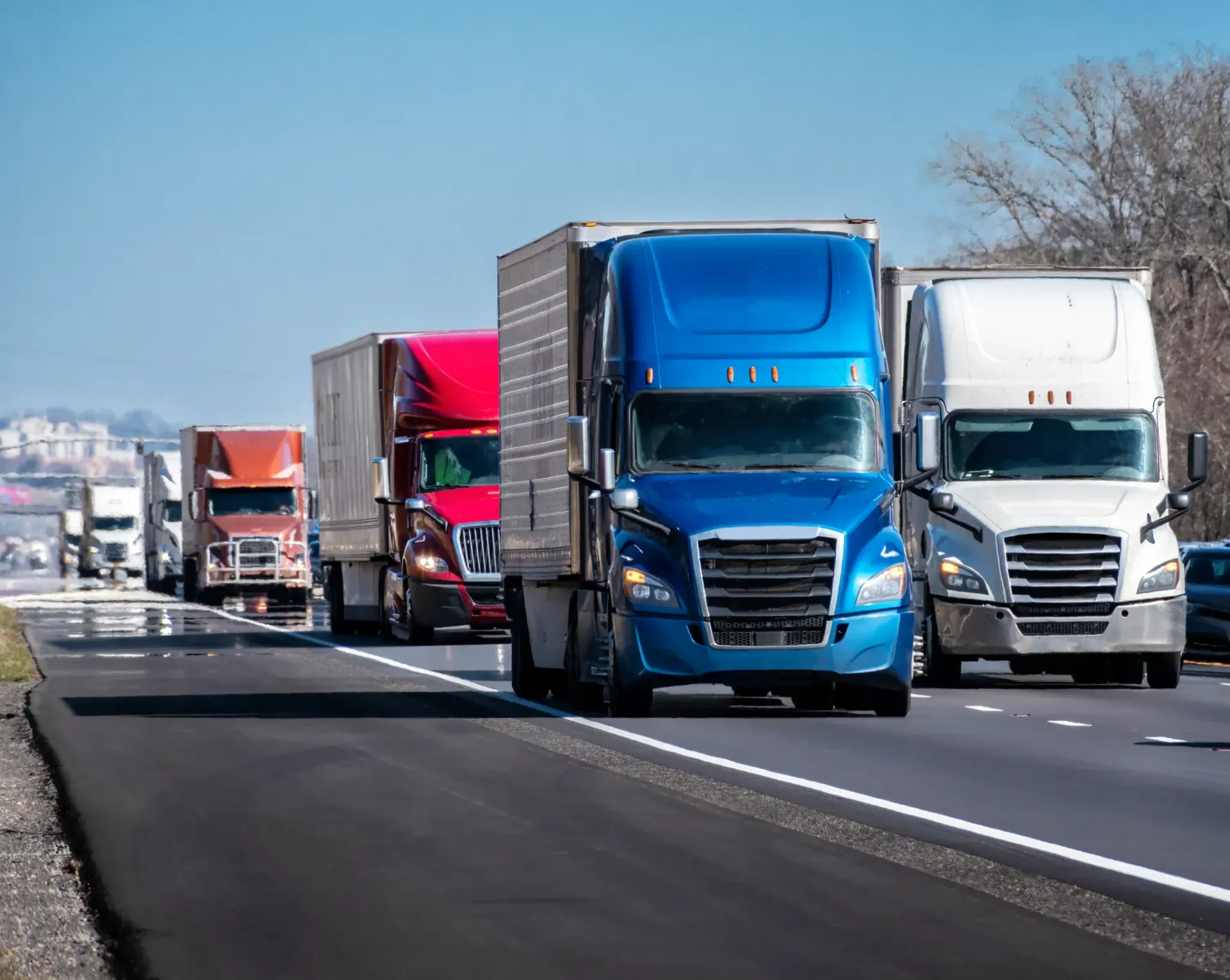 Semi-trucks driving on highway. Blue, red, and white trucks. Bright sunny day.
