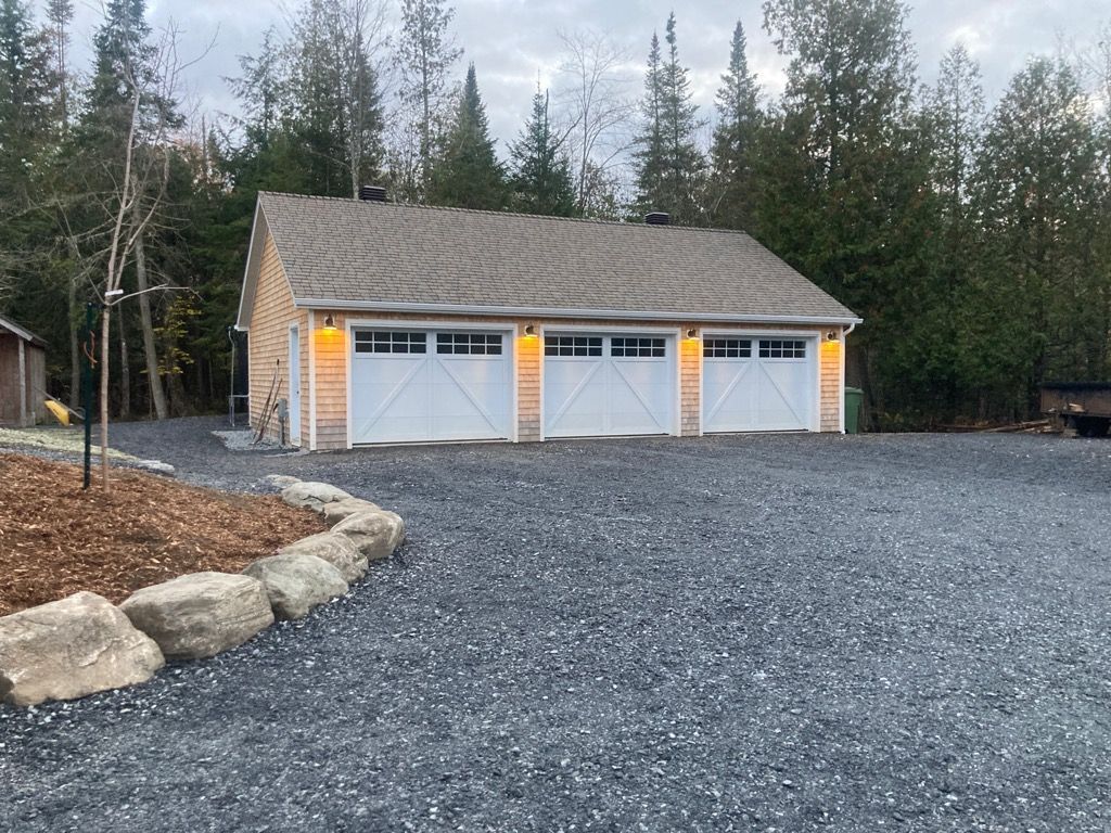 Un garage avec trois portes de garage se trouve au milieu d'une allée de gravier.
