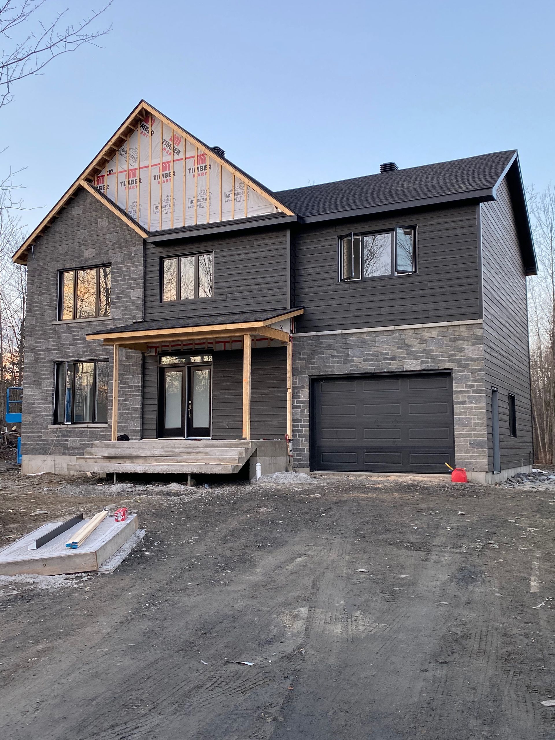 Une grande maison en briques avec une porte de garage noire est en construction.