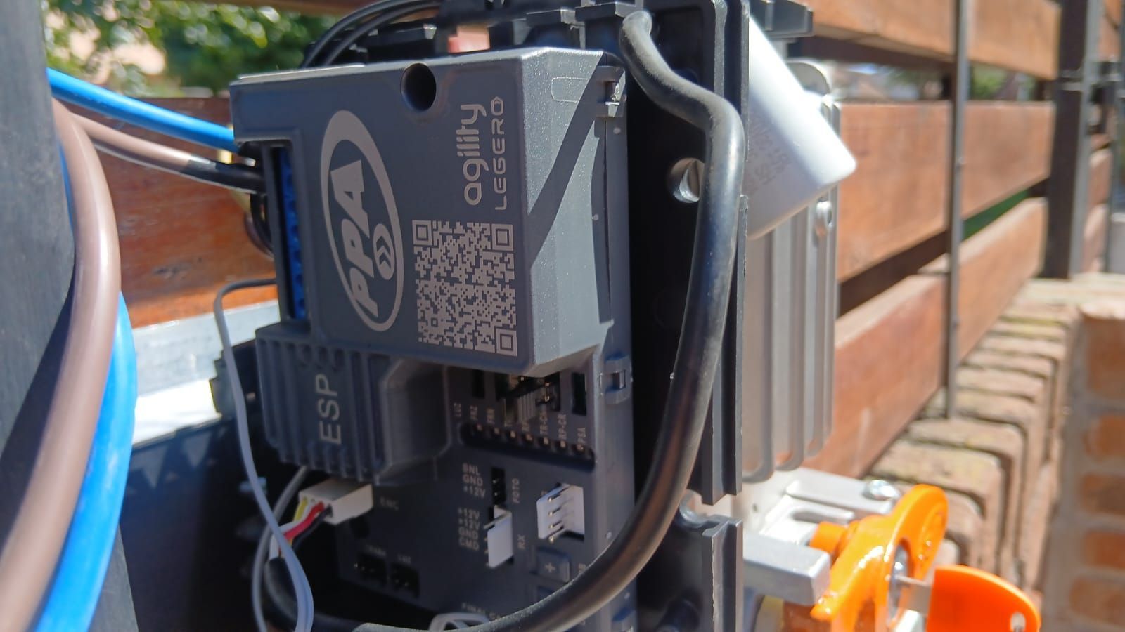 Una placa de control para motor de puerta PPA Agility, alojada en una carcasa de plástico gris oscuro, montada en una valla.